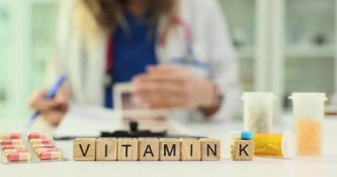 Tahta küplerin üzerinde K vitamini. Doktor masasında. Kadın doktorların belgelerini inceliyor. Sağlık ve ilaç takviyelerinin ağırdan alınması