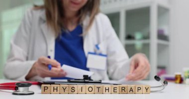 Fizyoterapist notlar alır ve tıbbi belgeleri tahta küplerle ilgili fizik tedavi kelimeleriyle doldurur. Kadın klinikte modern ekipmanlarla çalışıyor.