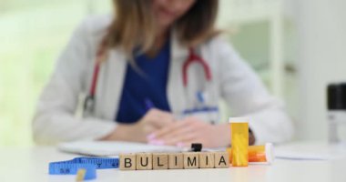 Doktor masasında mezura, mezura ve haplarla dolu ahşap küplerden oluşan bir kelime. Kadın aile terapisti klinikte yeme bozukluğu tedavisine yardımcı olur