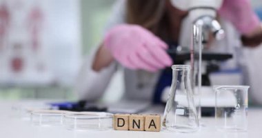 Tahta küplerin kısaltması DNA ve laboratuvarda çalışan bilim adamları. Kadın doktor tıbbi merkezde mikroskopla biyolojik materyal araştırması yapıyor.