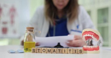 Kadın dişçi, masadaki belgelerle çalışıyor. Stomatitis ise tahta küplerle. Çenenin anatomik modeli diş ortamını önerir