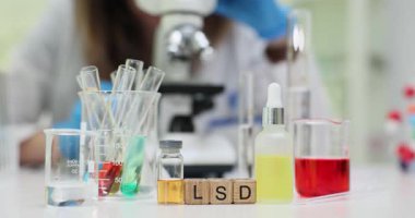 Kadın modern laboratuvarda renkli kimyasal maddeleri mikroskop altında LSD ile analiz ediyor. Test tüpleri LSD etkileri üzerine araştırma öneriyor