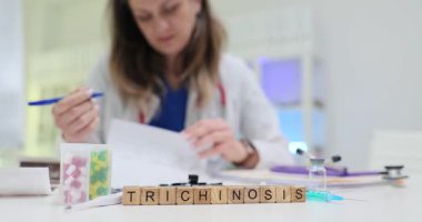 Uyuşturucu kapsüllerinin yakınındaki tahta blokların ve hastanedeki kadın doktorların trişinozunu yaz. Kadın sıhhiyeci muayenehanede hasta teşhisine odaklanıyor