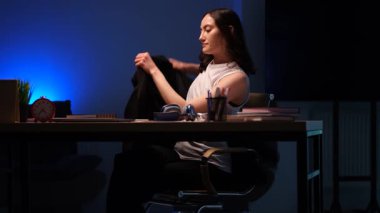 Genç bir kadın gece vardiyası için spor ceketini çıkarıyor. Kadın çalışan bilgisayarını açar ve iş yerindeki akıllı telefonu kontrol eder.