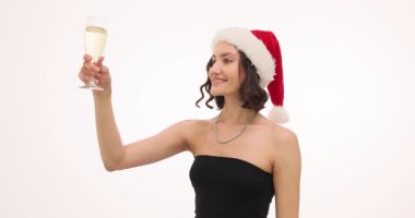 Noel Baba şapkalı gülümseyen genç kadın Noel 'i kutlamak için kadeh kaldırıyor. Beyaz arka planda neşeli yeni yıl partisi misafiri ağır çekimde