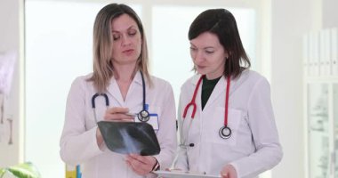 Kadın doktorlar göğüs röntgenini inceleyip hastanede teşhisi tartışıyorlar. Tıbbi uzmanlar hasta bakımı ve tedavi seçeneklerinde ağır çekimde işbirliği yaparlar.