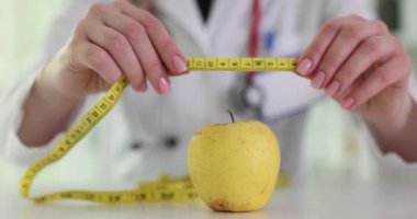 Doktor, masanın üzerindeki sarı elmanın etrafındaki şeritleri kullanıyor. Dengeli bir yaşam tarzı için sağlıklı beslenme ve kilo kaybı önemli