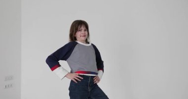 Eşofman altı ve kot pantolon giyen kız beyaz arka planda yumrukla tehdit ediyor. Oyuncu liseli kız somurtkan ifadesini yavaş çekimde gösteren kalçalarıyla el ele tutuşuyor.