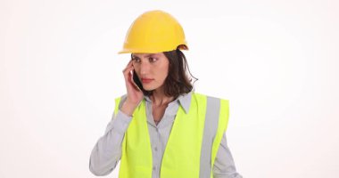 Güvenlik kaskı ve yelek giyen kadın mühendis cep telefonuyla konuşurken hayal kırıklığını ifade ediyor. Kadın beklenmedik haberler üzerine stres ve endişeyi gözler önüne seriyor