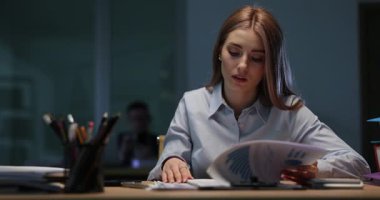 Genç bir kadın ofisinde geç saatlere kadar çalışıp mali belgeleri incelerken grafik ve çizelgeleri analiz ediyor. Baskı altında özveri ve odaklanma