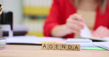 Ahşap küpleri, kadınlara karşı AGENDA kelimesi şeklinde sıralanmış. Deneyimli bir iş kadını, ağır çekim için kurul toplantıları ve görevler düzenler.