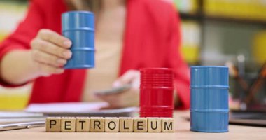 Keskin takım elbiseli iş kadını elinde minyatür yağ varilini tutuyor ve nakit sayıyor. Minyatür tahta küpler masanın üzerinde PETROLEUM sözcüğü oluşturur