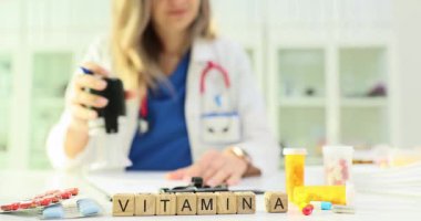 Minyatür tahta küpler masada VITAMIN A kelimesini oluşturur. Deneyimli hekim ilave tavsiyeler yazar ve reçeteli belgeyi damgalar