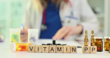 Doktor küplere PP vitamini reçetesi yazıyor. Sıvı ilaçlarla dolu ampuller ve masanın üzerine yerleştirilmiş renkli haplar.