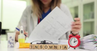 Deneyimli kadın sağlık çalışanı randevudayken hasta kayıtlarını dikkatlice inceler. Ahşap bloklar InSOMNIA düzgün sıralanmış masanın kenarında