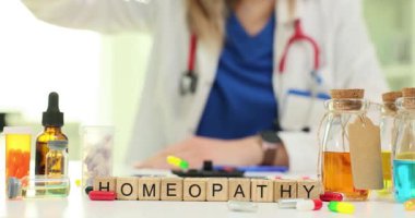 Homeopati doktoru küçük konteynırlardan renkli tabletleri masaya döker. Tahta küpler kelime oluşturma HOMEOPATHY masa yavaş çekim düzgün sıralanmış