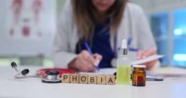 İlaç ve steteskop yanında tahta küplerin yazılı fobisi. Kadın doktor klinikte akıl sağlığı bozukluğu reçetesi yazıyor.