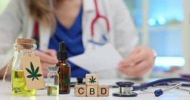 Kadın doktor, tıbbi kenevir CBD yağı için ilaç içeren şişelerle reçete yazıyor. Reçeteye beklenen tedavi etkilerinin açıklaması da dahil.