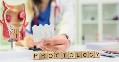 Kadın proktolog, masa başında kelime proktolojisine göre bir dizi fitil gösteriyor. Doktor anal çatlakların belirtilerini tartışıyor ve uygun ilaçları tutuyor.