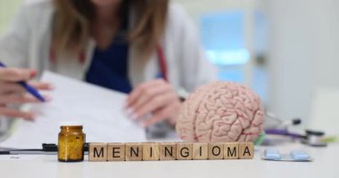 Kadın doktor, tıp bürosunda Meningiyom 'lu ahşap bloklarla çevrili belgelerle özenle çalışıyor. Beyin modeli klinik ayarları öneriyor