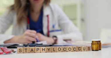 Kadın doktor, tahta küplerin yanında Staphylococcus ve ilaç şişeleriyle reçete yazıyor. Klinik ortamında enfeksiyon tedavisi