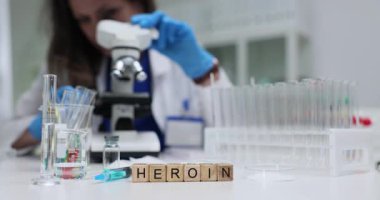 Tıp laboratuarında şırınga ve kimyasallarla ahşap küplerle ilgili kelime eroini. Kadın bilim adamı laboratuardaki masada mikroskop kullanarak ilaçları analiz ediyor.