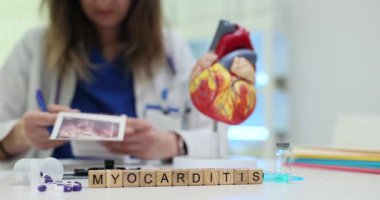 Doktorun yanında kalp mankeni olan tahta blokların miyokarditi. Kadın doktor, hastane ofisindeki hastanın ultrason taraması fotoğraflarını inceliyor.