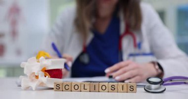 Doktor masasında omurgalar arası disk modeli olan tahta küplerin skolyozu. Kadın doktor klinikteki randevusunda tıbbi rapor yazıyor.