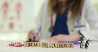 Kadın doktor, immünoloji sözcüğünün yanında tıbbi çalışma alanının üzerinde dinlenen tahta bloklara tıbbi notlar yazıyor. Bağışıklık sisteminin incelenmesi ve tedavisi