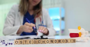 Doktor, insan omurgasının anatomik modeline karşı kemik erimesi üzerine tıbbi rapor yazıyor. Hasta bakımı ve tedavi seçenekleri