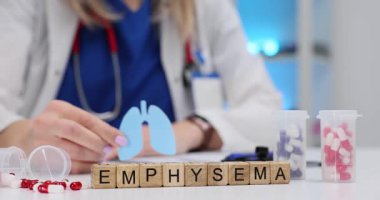 Kadın doktor amfizem kelimesinin yanında tahta küplerin üzerinde kağıt ciğerler tutuyor. Randevu sırasında kronik obstrüktif akciğer hastalığının tedavisi ve önlenmesi