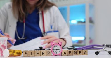 Kadın doktor, Uyku Apnesi tedavisi için dikkatlice reçete yazıyor. Doktor, hastaya normal uyku saatleri için çalar saati ayarlamasını tavsiye ediyor.