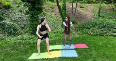 Açık havada egzersiz yapan sporcu kadınlar parktaki çimenlikteki renkli spor minderlerinde çömelme hareketleri yapıyorlar. Green Park 'ta koçun rehberliğinde birlikte antrenman yapıyoruz.