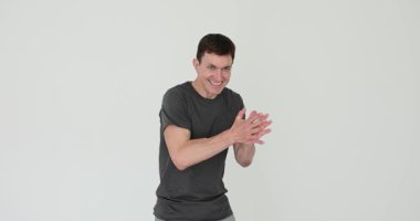 Tişört giyen adam beyaz arka planda gülümseyen elleri ovalıyor. Canning erkeği stüdyoda hareketli şeytani planlar yapar. Duyguların ifadesi