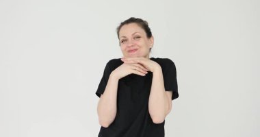 Siyah tişörtlü bir kadın beyaz arka planda sevimli bir yüzün yanında el ele tutuşurken gülümsüyor. Flört eden kadın başını eğdi, yüzünü buruşturdu ve olumlu duygularını ifade etti.