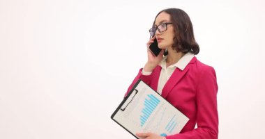 Gözlüklü bir iş kadını elinde iş çizelgesiyle telefon görüşmesi yapıyor. Meşgul bayan patron beyaz arka planda yavaş çekimde anlaşmayı tartışıyor.