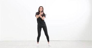 Siyah spor giysili genç bir kadın stüdyoda enerjik bir şekilde dans ediyor. Uzun saçlı bayan, hip hop ve aktif yaşam tarzına olan tutkusunu gösteriyor.