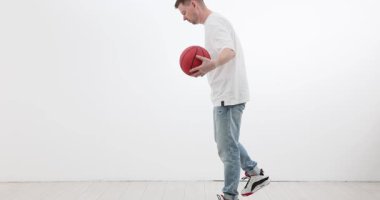 Adam beyaz arka planda basketbol topu sürme becerisi geliştiriyor. Erkek sporcu spor müsabakalarına ve ağır çekimde atletik adanmışlığa katılır.