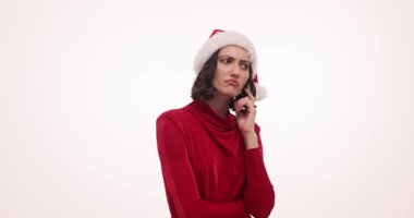 Noel Baba şapkalı genç bir kadın beyaz arka planda düşünüyor ve kafasına vuruyor. Kırmızı elbiseli bayan ailesi ve arkadaşları için Noel hediyeleri arıyor.