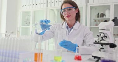Kadın bilim adamı laboratuardaki araştırma sırasında deney kabına mavi sıvı döküyor. Kadın kimyager laboratuvarda sıvı reaksiyonlarını inceliyor.