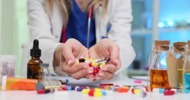 Kadın doktor masasında bir avuç renkli hap ve kapsül tutuyor. Eczacı tıbbi araştırma ve yeniliğin önemini gösteriyor