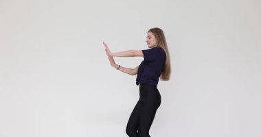 Genç bir kadın kollarını açarak enerji ve mutlu bir ifadeyle dans eder. Bayan beyaz arka planda ritim ve dans özgürlüğünden hoşlanır.