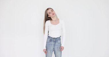 Uzun sarı saçlı genç bir kadın boynu esnesin diye başını sağa sola eğiyor. Beyaz stüdyoda fotoğraf çekimi sırasında kasları gevşet ve gerginliği at.