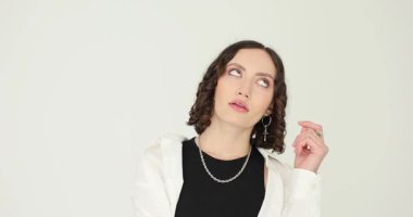 Kadın yukarı bakıyor, elleri nazikçe çenesine dokunuyor ve derin düşüncelere dalıyor. Kadın ifadesi düşünmeyi ve cevabı aramayı önerir.