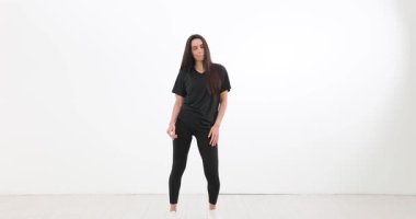 Dansçı kadın, siyah atletik kıyafetler giyerek beyaz stüdyoda çağdaş koreografi sergiliyor. Dinamik hareket ve sanatsal tutku yavaş çekim