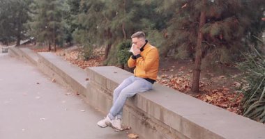 Adam parkta alçak duvarda oturup ağaçlarla çevrili sonbahar alerjilerinden muzdarip dokuyla burun siliyor. Düşen kahverengi yapraklar soğuk mevsimi akla getiriyor.