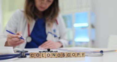 Doktor, masadaki tahta küplere kolonoskopi prosedürü hakkında tıbbi rapor yazıyor. Hastanede hasta bakımı ve teşhisin önemi