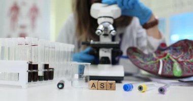 Tahta küplerle ilgili mektuplar ve laboratuvarda kan örnekleri ve karaciğer modeli. Kadın araştırmacı mikroskopla aspartam amino transferaz testi yapıyor.