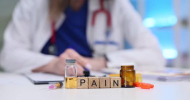 Tahta bloklarda ağrı var. Masada doktorlara karşı ilaçlar var. Kadın terapist ağrı kesiciler için reçete yazıyor.