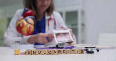 Endokardit 'i tahta bloklara, kalp modelini de doktor masasına yaz. Kadın doktor, muayene odasındaki ultrason görüntülerini inceliyor.
